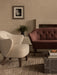 A cream Ingeborg Lounge Chair and a burgundy sofa in a living room with a marble plinth coffee table and a jute rug.