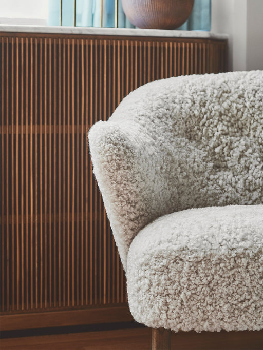 A close-up of the Ingeborg Lounge Chair's plush, off-white sheepskin upholstery against a dark, fluted wood cabinet.
