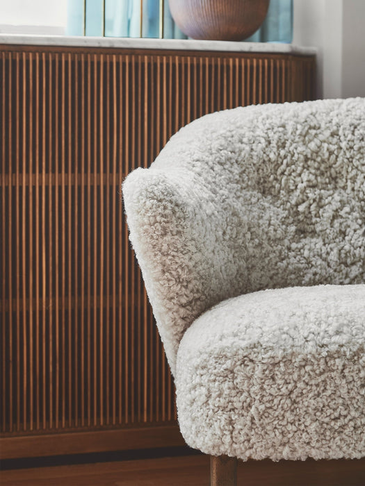 A close-up of the Ingeborg Lounge Chair's plush, off-white sheepskin upholstery against a dark, fluted wood cabinet.