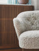 A close-up of the Ingeborg Lounge Chair's plush, off-white sheepskin upholstery against a dark, fluted wood cabinet.