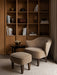 A beige Ingeborg Lounge Chair and Ingeborg Ottoman sit on a striped rug in front of a large wooden shelving unit.
