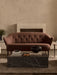 The Ingeborg Sofa in brown fabric shown in a living room with a black marble Plinth Low coffee table in front of a fireplace.