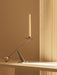 The small, sculptural Interconnect Candle Holder in polished steel holds a cream candle on a shelf in warm, soft light.