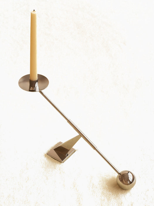 Audo Interconnect Candle Holder, Small, in polished steel, a sculptural piece balancing a beige candle on a cream surface.