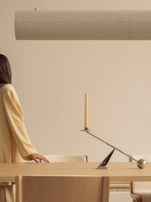 Woman at a dining table with an Interconnect Candle Holder, below a Hashira Linear Pendant, with Ready Dining Chairs nearby.