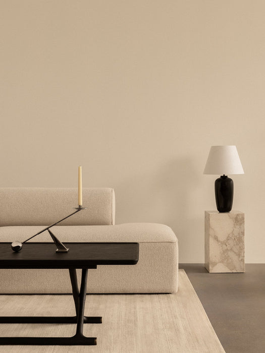 A minimalist room with an Eave Sofa, Jager Table with Interconnect Candle Holder, and Torso Lamp on a tall marble Plinth.
