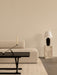 A minimalist room with an Eave Sofa, Jager Table with Interconnect Candle Holder, and Torso Lamp on a tall marble Plinth.