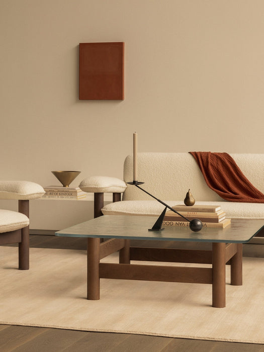 A modern living room with a cream bouclé sofa, glass coffee table with a sculptural black candlestick, and warm earthy tones.