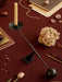 Overhead view of the black Audo Interconnect Candle Holder on a red tablecloth, styled with dried flowers, books and pearls.