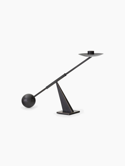 A sculptural dark bronze candlestick, its long arm balancing on a pyramidal base, with a sphere at one end and a holder.