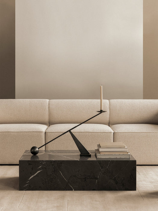 A black marble Plinth Low table in front of an Eave Modular Sofa. On the table is an Interconnect Candle Holder and books.
