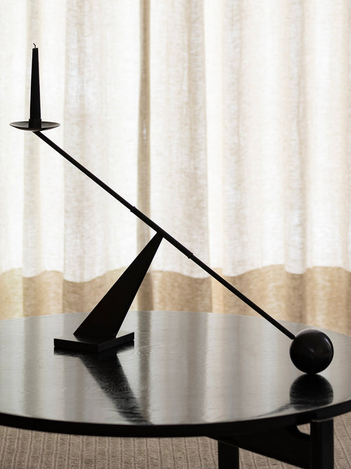A sculptural black Interconnect Candle Holder with a matching black candle, balanced on a black wooden Passage Lounge Table.