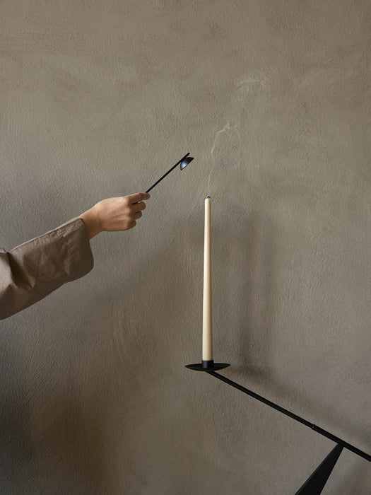 A hand holding a black candle snuffer extinguishes a cream tapered candle in the black metal Interconnect Candle Holder.
