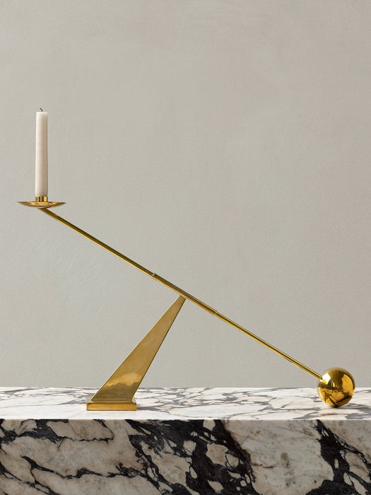 The polished brass Interconnect Candleholder with a white candle, resting on a black and white marble Plinth Low.