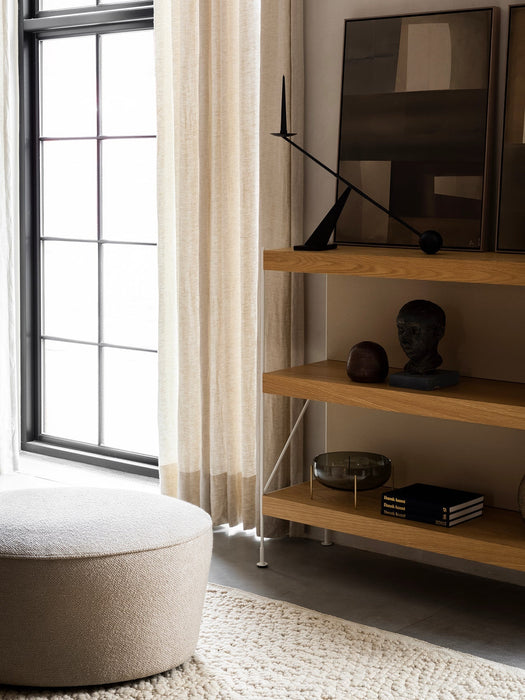 An oak Zet Storage System with an Interconnect Candle Holder and Echasse Bowl. A Cairn Pouf and Gravel Rug are by a window.