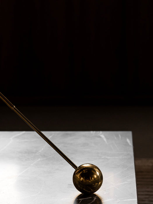 Close-up detail of the Interconnect Candle Holder's polished brass sphere and stem resting on a grey marble surface.
