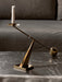 The brass Interconnect Candle Holder, with a white candle, rests on a black marble surface, resembling a balance scale.