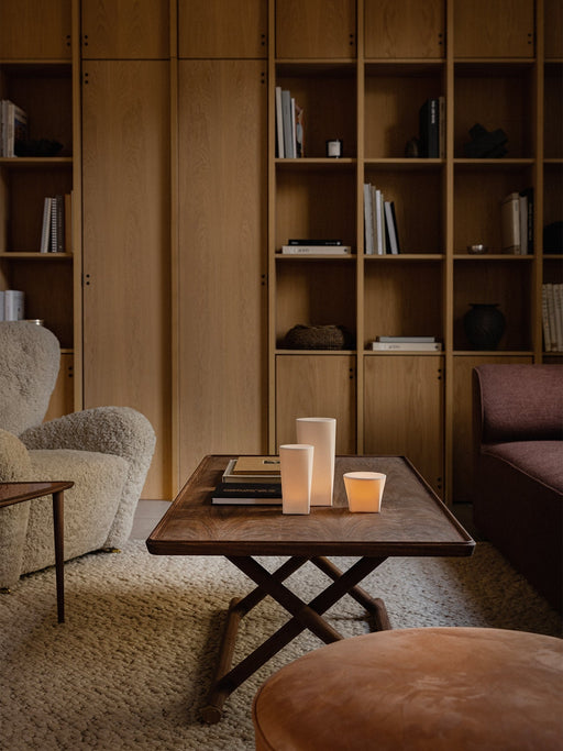 A Jäger Lounge Table with Ignus Candles, beside a Tired Man armchair and Cairn Pouf in a cosy, wood-panelled living room.