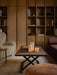 A Jäger Lounge Table with Ignus Candles, beside a Tired Man armchair and Cairn Pouf in a cosy, wood-panelled living room.