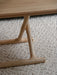 Close-up of the Jäger Lounge Table's natural oak legs with brass fittings, showing the criss-cross design on a cream rug.