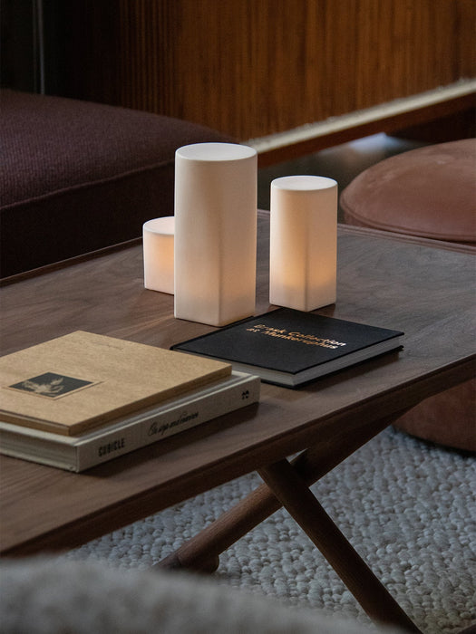 A close-up of the wooden Jäger Lounge Table, styled with books and three glowing Ignus Flameless Candles on a white rug.