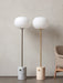 The JWDA Floor Lamp in two variations: white marble with a bronzed brass stem and travertine with a brushed brass stem.