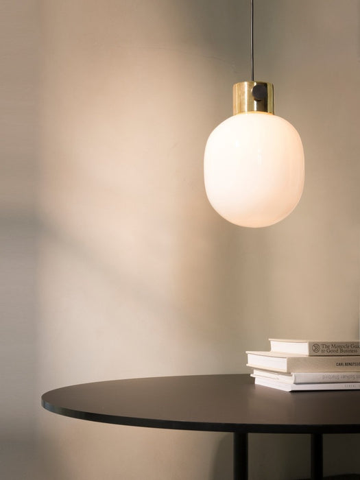 The illuminated JWDA Metallic Pendant Lamp in polished brass hangs above a black table on which rests a stack of three books.