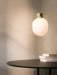 The illuminated JWDA Metallic Pendant Lamp in polished brass hangs above a black table on which rests a stack of three books.