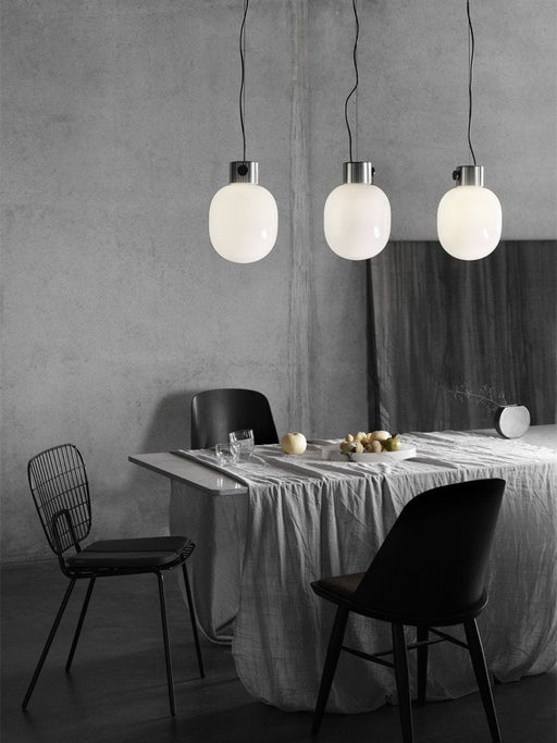 Three JWDA Metallic Pendant Lamps by Jonas Wagell hanging over a dining table in a minimalist, modern Danish design setting.