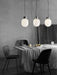 Three JWDA Metallic Pendant Lamps by Jonas Wagell hanging over a dining table in a minimalist, modern Danish design setting.