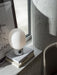 The JWDA Table Lamp, with a marble base and opal glass shade, styled on a stack of books on a sunlit concrete windowsill.