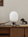 The JWDA Table Lamp in Calacatta Viola marble sits on a dark wood cabinet, styled with a book and abstract sculptures.