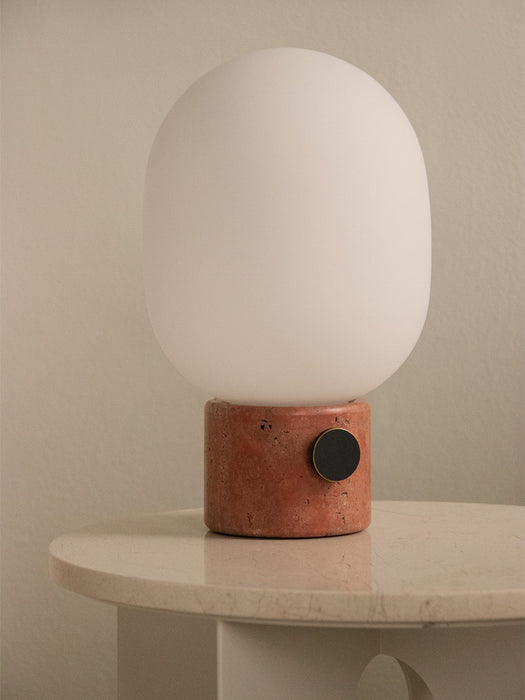 Close-up of the JWDA Table Lamp with red travertine base and opal glass shade, resting on the Androgyne Side Table.