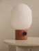 Close-up of the JWDA Table Lamp with red travertine base and opal glass shade, resting on the Androgyne Side Table.