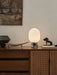 The JWDA Table Lamp in Calacatta Viola marble, lit on a wood sideboard with rattan doors, styled with art and sculptures.