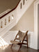 The Knitting Lounge Chair in sheepskin, with its dark wooden frame, sits on a tiled floor by a grand, white staircase.