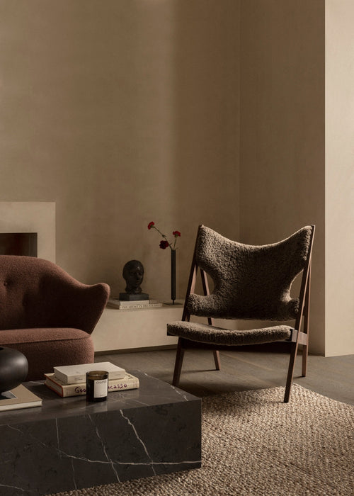 The brown sheepskin Knitting Lounge Chair in a modern room with a marble Plinth table, Ingeborg Sofa, and Stance Vase.