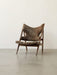 A side view of the Knitting Lounge Chair, upholstered in thick brown sheepskin with a dark wooden frame, on a grey floor.