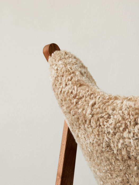 A close-up of the Knitting Lounge Chair, highlighting the fluffy sheepskin upholstery and the smooth, warm wooden frame.