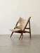 A Knitting Lounge Chair in light Sheepskin with a dark wood frame, viewed from the side on a grey floor against a white wall.