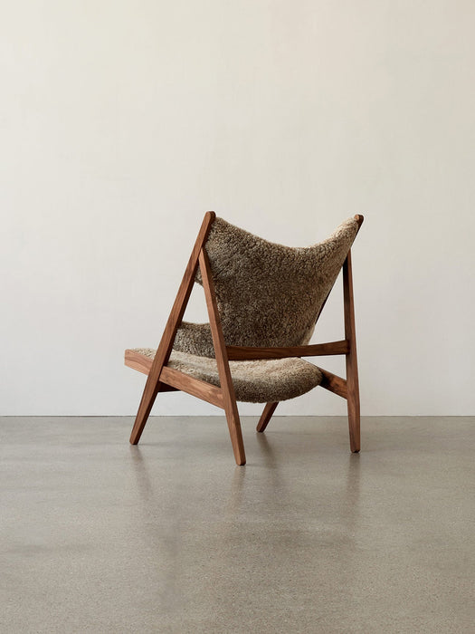Three-quarter back view of the Knitting Lounge Chair in brown Sheepskin with a dark wood frame, set in a minimalist room.