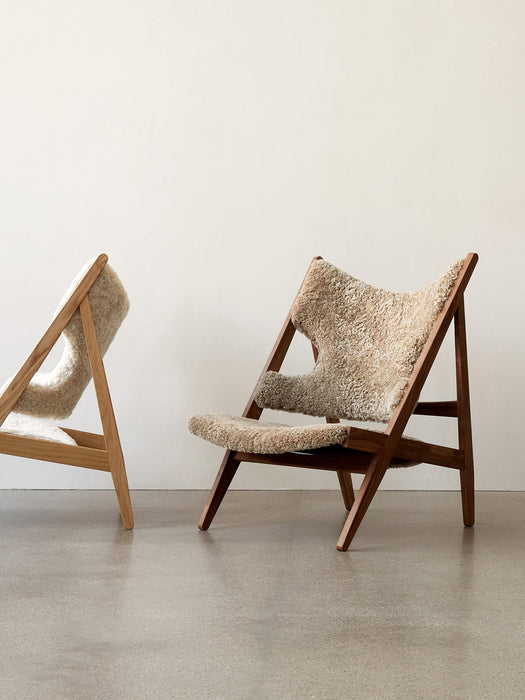 Two Knitting Lounge Chairs in Sheepskin, one dark wood frame, one light wood frame, in a minimalist interior.