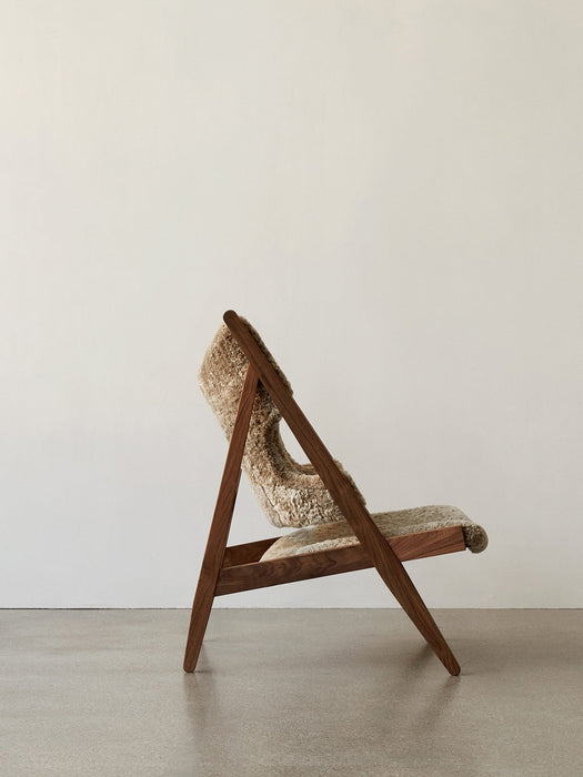 Side view of the Knitting Lounge Chair, Sheepskin, with its dark walnut A-frame and plush, light brown sheepskin upholstery.