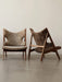 Two Knitting Lounge Chairs in sheepskin with wood frames, one light brown & one dark brown, against a plain off-white wall.