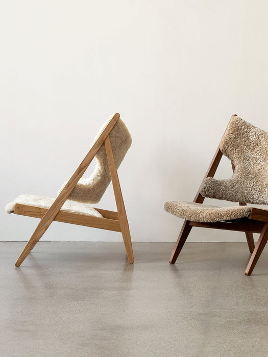 Side profile of the Knitting Lounge Chair with a natural oak frame and off-white Sheepskin in a bright, modern room.