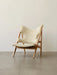 A side-angle view of the Knitting Lounge Chair in natural oak with off-white sheepskin upholstery, against a white wall.