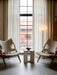 Two Knitting Lounge Chairs in Sheepskin flank an Androgyne Side Table in a living room with a tall window and a JWDA Lamp.