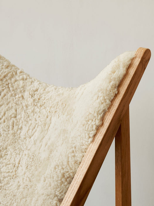 Close-up detail of the Knitting Lounge Chair, showing the fluffy white sheepskin seat set within the solid natural oak frame.