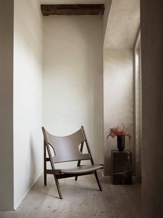 The leather and wood Knitting Lounge Chair in a hallway, next to a marble Plinth holding a Cyclades Vase with red foliage.