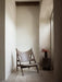 The leather and wood Knitting Lounge Chair in a hallway, next to a marble Plinth holding a Cyclades Vase with red foliage.